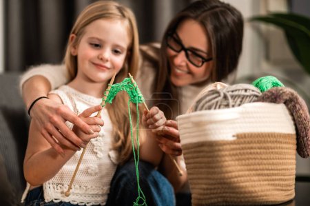 Photo for Cheerful mother and little daughter knitting together while having leisure time - Royalty Free Image