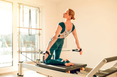 Téléchargez les photos : Femme flexible et mince faisant des exercices d'étirement sur la machine Pilates dans le studio de yoga - en image libre de droit