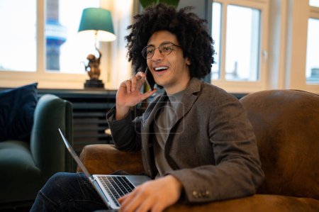Foto de Trabajar en línea. Joven sonriente rizado hombre pasar tiempo en línea - Imagen libre de derechos