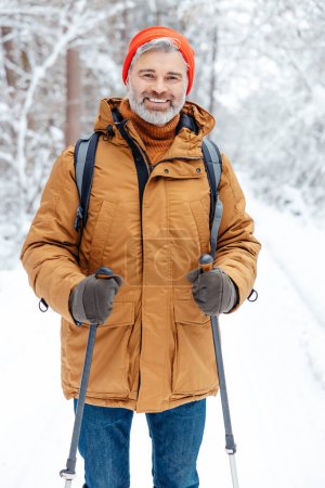 Man in a winter forest. Smiling mature man in red hat in a snowy forest