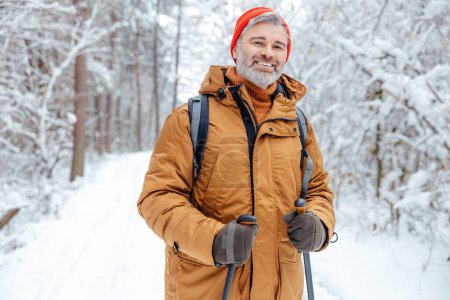 Man in a winter forest. Smiling mature man in red hat in a snowy forest