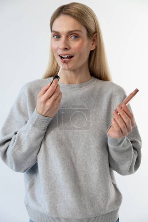 Téléchargez les photos : Maquille. Jeune femme blonde tenant du rouge à lèvres dans les mains - en image libre de droit