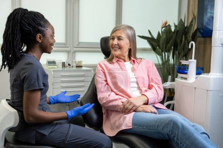 Téléchargez les photos : Une dentiste multiculturelle consulte une femme d'âge moyen dans une clinique de stomatologie - en image libre de droit