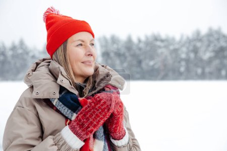 Foto de Té para mantener el calor. Sonriente mujer madura en sombrero rojo teniendo té caliente al aire libre - Imagen libre de derechos