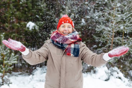 Téléchargez les photos : Météo enneigée. Heureuse femme mûre profitant du temps neigeux dans une forêt - en image libre de droit