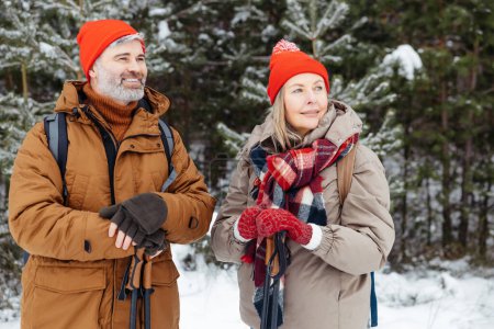 Téléchargez les photos : Loisirs d'hiver. Mature homme et femme debout dans une forêt d'hiver et regardant satisfait - en image libre de droit