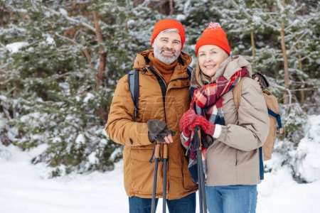 Photo for Winter leisure. Mature man and woman standing in a winter forest and looking contented - Royalty Free Image