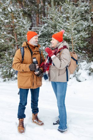 Téléchargez les photos : Du thé chaud. Sourire couple d'âge mûr ayant du thé chaud dans une forêt d'hiver - en image libre de droit
