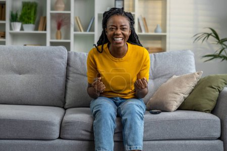 Téléchargez les photos : Jeune femme afro-américaine assise sur le canapé chez elle - en image libre de droit