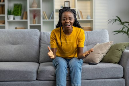 Téléchargez les photos : Jeune femme en t-shirt jaune assis sur le canapé et l'air excité - en image libre de droit