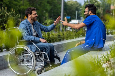 Foto de Me siento bien. Enfermera masculina en médicos azules en general estrechando la mano con un paciente en silla de ruedas - Imagen libre de derechos
