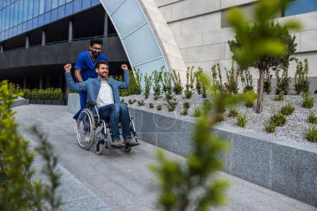 Foto de Incapacidad. Hombre guapo sentado en una silla de ruedas mientras pasea con una enfermera - Imagen libre de derechos