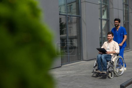 Photo for In a hospital. Disabled man having a walk with a male nurse and reading his prescription leaflet - Royalty Free Image