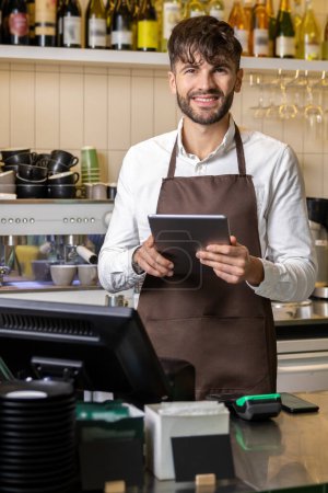 Téléchargez les photos : Homme heureux ou serveur dans tablier avec tablette PC au bar ou café - en image libre de droit