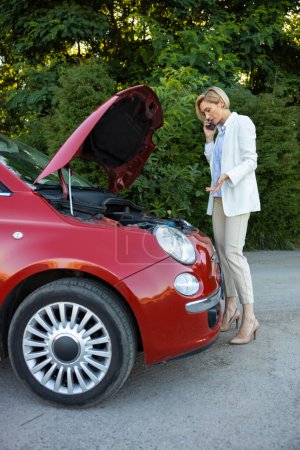 Téléchargez les photos : Jeune femme utilisant un téléphone portable pour appeler au service pour réparer sa voiture tout en restant debout sur la route - en image libre de droit