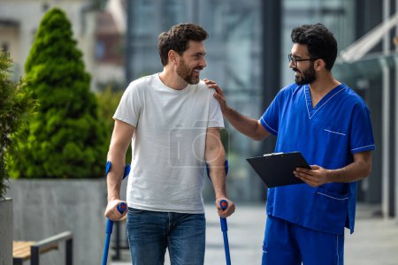 Photo for Walk together. Man with crutches and a male nurse talking friendly on a walk - Royalty Free Image