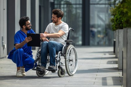 Foto de Hombre sentado en una silla de ruedas y discutiendo algo con un enfermero - Imagen libre de derechos