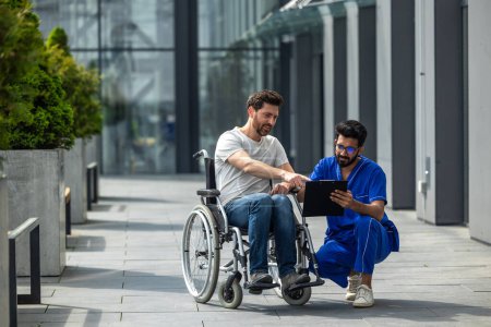 Photo for Man sitting in a wheelchair and discussing something with male nurse - Royalty Free Image