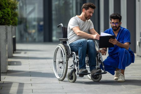 Foto de Hombre sentado en una silla de ruedas y discutiendo algo con un enfermero - Imagen libre de derechos