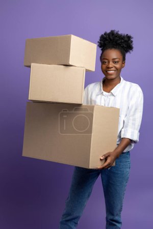 Téléchargez les photos : Au travail. Jeune femme à la peau foncée avec des boîtes dans les mains semblant satisfaite - en image libre de droit