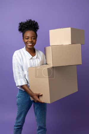 Foto de En el trabajo. Mujer joven de piel oscura con cajas en las manos que parecen contentas - Imagen libre de derechos
