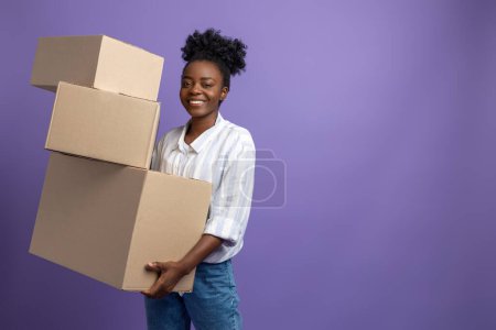 Foto de En el trabajo. Mujer joven de piel oscura con cajas en las manos que parecen contentas - Imagen libre de derechos