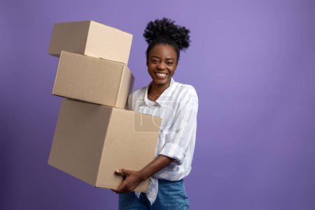 Photo for At work. Dark-skinned young woman with boxes in hands looking contented - Royalty Free Image