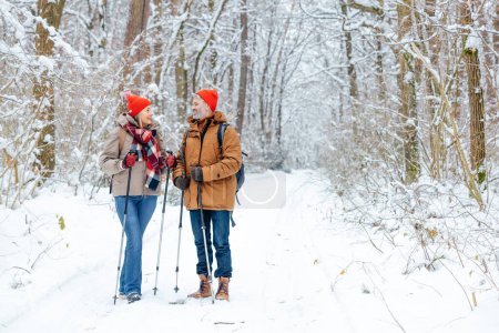Active people. Mature couple having a walk in a snowy forest with scandinavian sticks