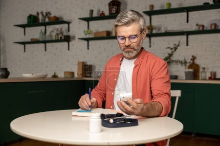 Photo for Gray haired middle aged man with glucometer checking blood sugar level taking notes with indicators in notepad at home - Royalty Free Image