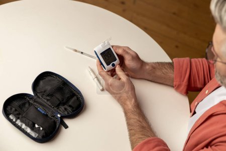 Téléchargez les photos : Homme diabétique malsain vérifiant le taux de sucre dans le sang avec glucomètre à la maison - en image libre de droit