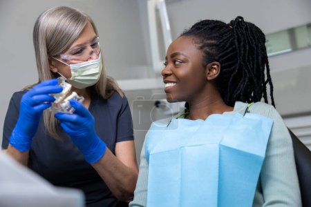 Mujer dentista mostrando prótesis dentales en clínica