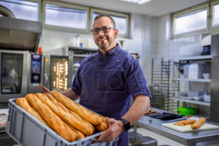 Photo for Smiling man employee holding baguettes at commercial bakery - Royalty Free Image