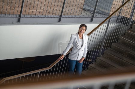 Foto de Mujer en las escaleras. Mujer con chaqueta blanca y jeans en las escaleras del edificio de oficinas - Imagen libre de derechos