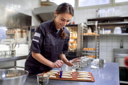 Téléchargez les photos : Cuisinière en uniforme préparant des croissants dans la cuisine de la boulangerie - en image libre de droit