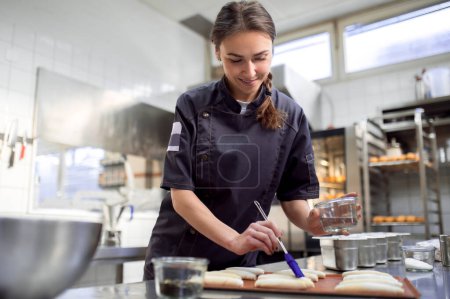 Photo for Female baker in uniform preparing croissants in bakehouse kitchen - Royalty Free Image