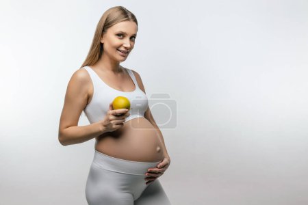 Foto de Nutrición saludable. Sonriente rubia embarazada con manzana en las manos - Imagen libre de derechos