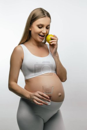 Foto de Una mujer embarazada. Mujer embarazada de pelo largo sosteniendo manzana en la mano y sonriendo - Imagen libre de derechos
