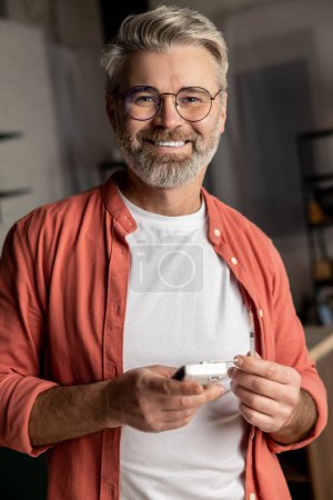 Smiling diabetic man holding checking blood sugar level glucometer in home interior