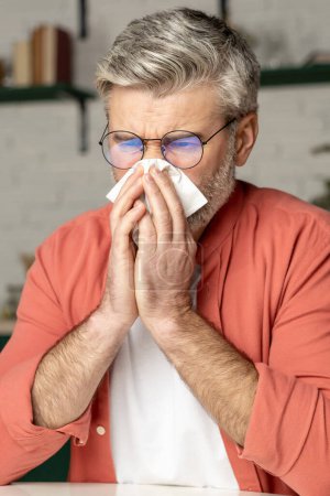Téléchargez les photos : Homme malsain éternuer avec mouchoir souffrant de grippe froide posant à l'intérieur de la maison - en image libre de droit