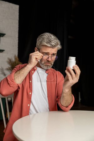 Photo for Caucasian sick unhealthy man with bottle of pills reading method of administration and dosage of the medicine - Royalty Free Image