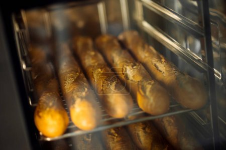 Téléchargez les photos : Cuisson de baguettes fraîches croustillantes au four à la boulangerie commerciale - en image libre de droit