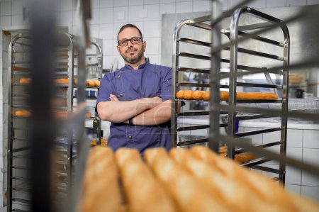 Foto de Hombre panadero en uniforme con bandejas de pan fresco en panadería. - Imagen libre de derechos