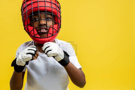 Téléchargez les photos : Petit combattant afro-américain en casque de boxe protecteur et gants isolés sur fond jaune - en image libre de droit