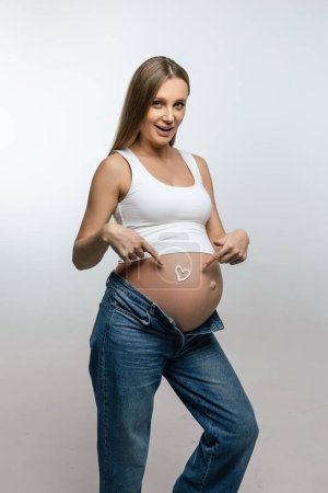 Foto de Crema anti-estiramiento. Embarazada poniendo crema en su vientre y buscando disfrutado - Imagen libre de derechos