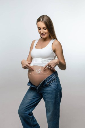 Téléchargez les photos : Crème anti-stretch. Femme enceinte mettre de la crème sur le ventre et regarder apprécié - en image libre de droit
