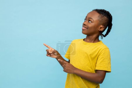 Foto de Feliz niño de piel oscura indicando en el área de publicidad aislado sobre fondo azul - Imagen libre de derechos