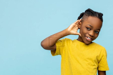 Foto de Sonriente niño afroamericano con la mano cerca de la oreja aislado sobre fondo azul, espacio de copia - Imagen libre de derechos