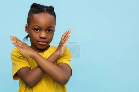 No way. Serious dark- skinned little boy with crossed hands isolated over blue background, copy space