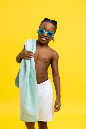 Photo for Swimming time. Cute african american boy in swimming eyeglasses and with towel on his shoulder - Royalty Free Image