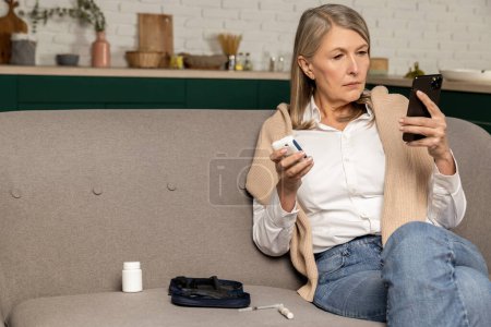Photo for Blood sugar measurement. Mature woman checking glucometer results on internet and looking involved - Royalty Free Image